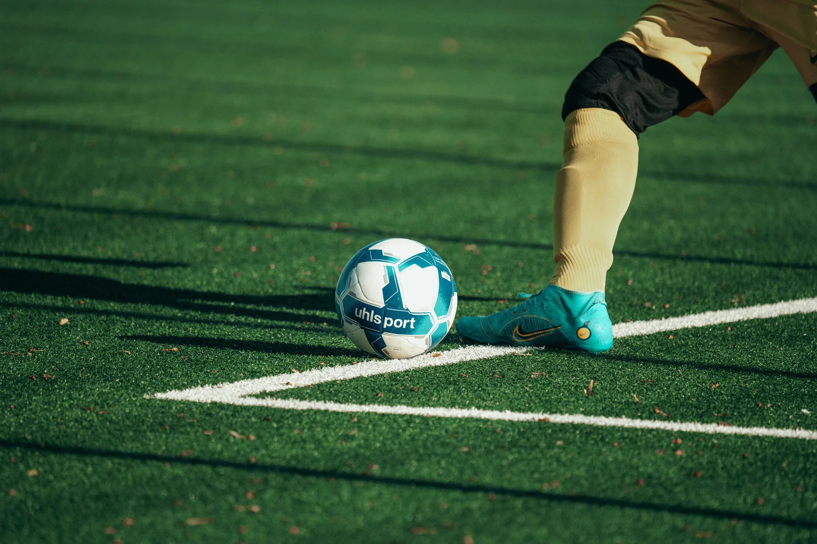 Bota de fútbol junto a un balón en césped artificial