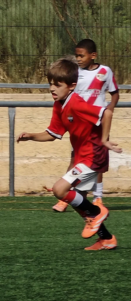 Niño jugando al fútbol en césped artificial con botas adidas Predator